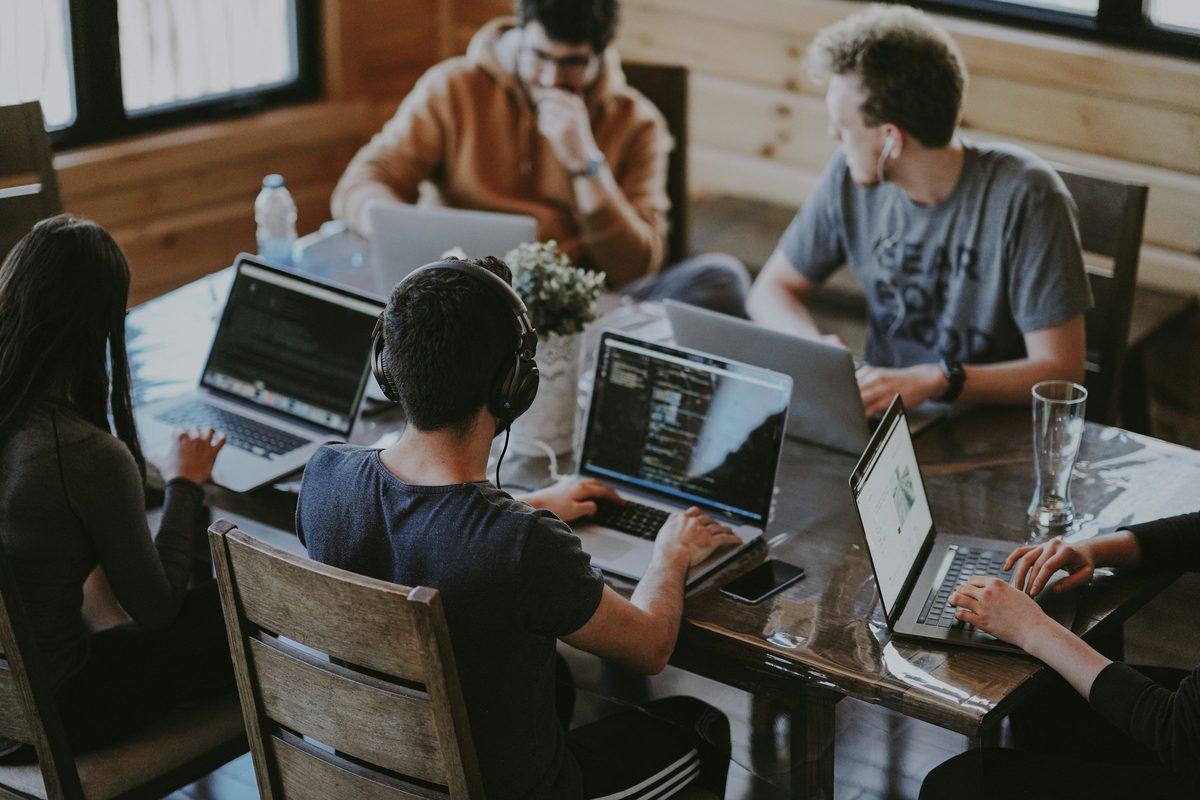Five people working around a long table on open laptops, one screen filled with an open code editor