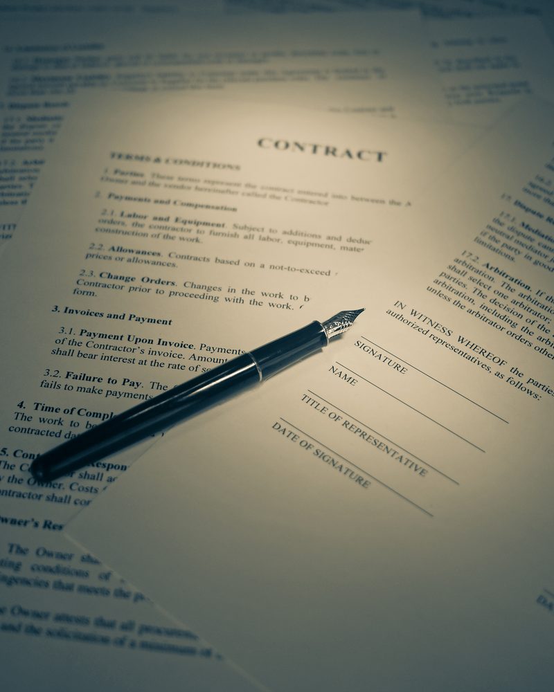 A printed contract open at its terms and conditions and signature block, a fountain pen lying across the page