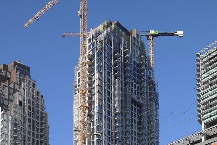 Two high rise towers under construction against a clear blue sky, tower cranes standing over the unfinished upper floors